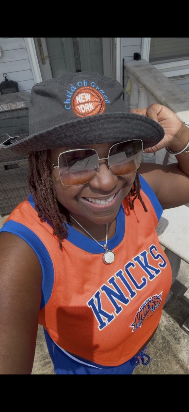 Model in a New York Knicks jersey wearing a black embroidered CHILD OF GRACE bucket hat